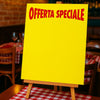 Cartello per offerte, giallo con scritta rossa OFFERTA SPECIALE, mostrato sui tavolo di una pizzeria