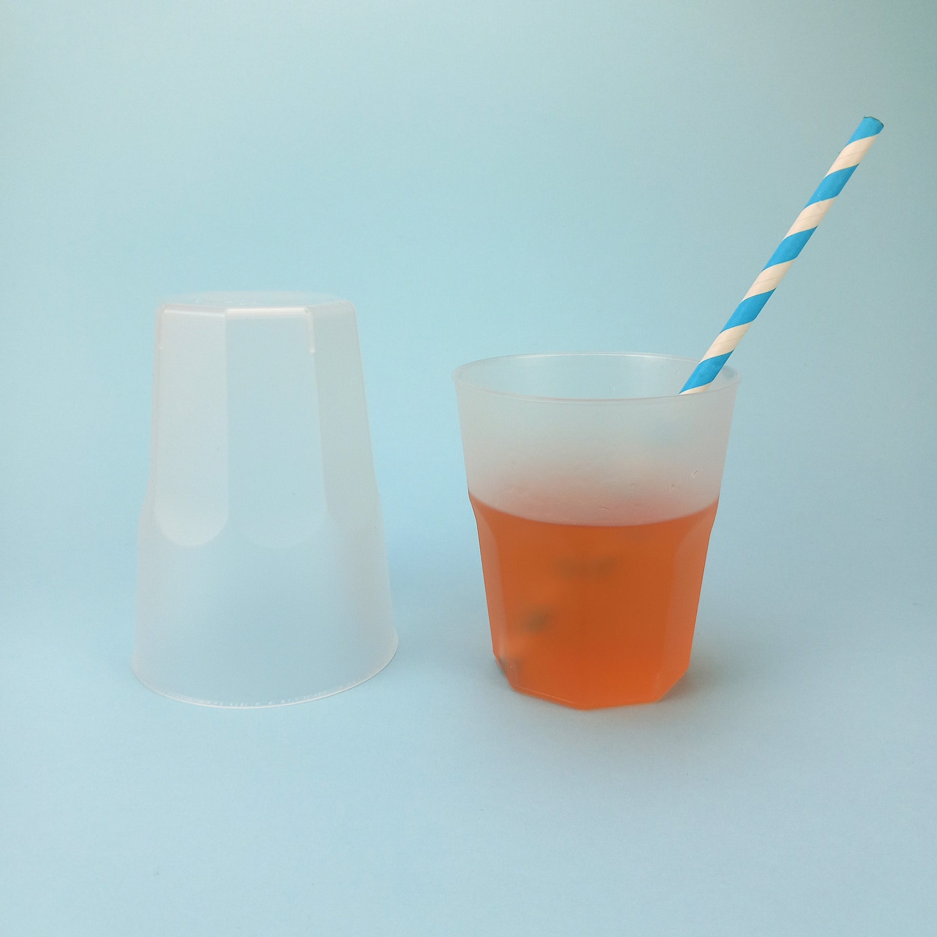 Bicchiere di plastica, opaco, monouso , uno capovolto ed uno pieno di te con cannuccia a righe bianco e azzurre 