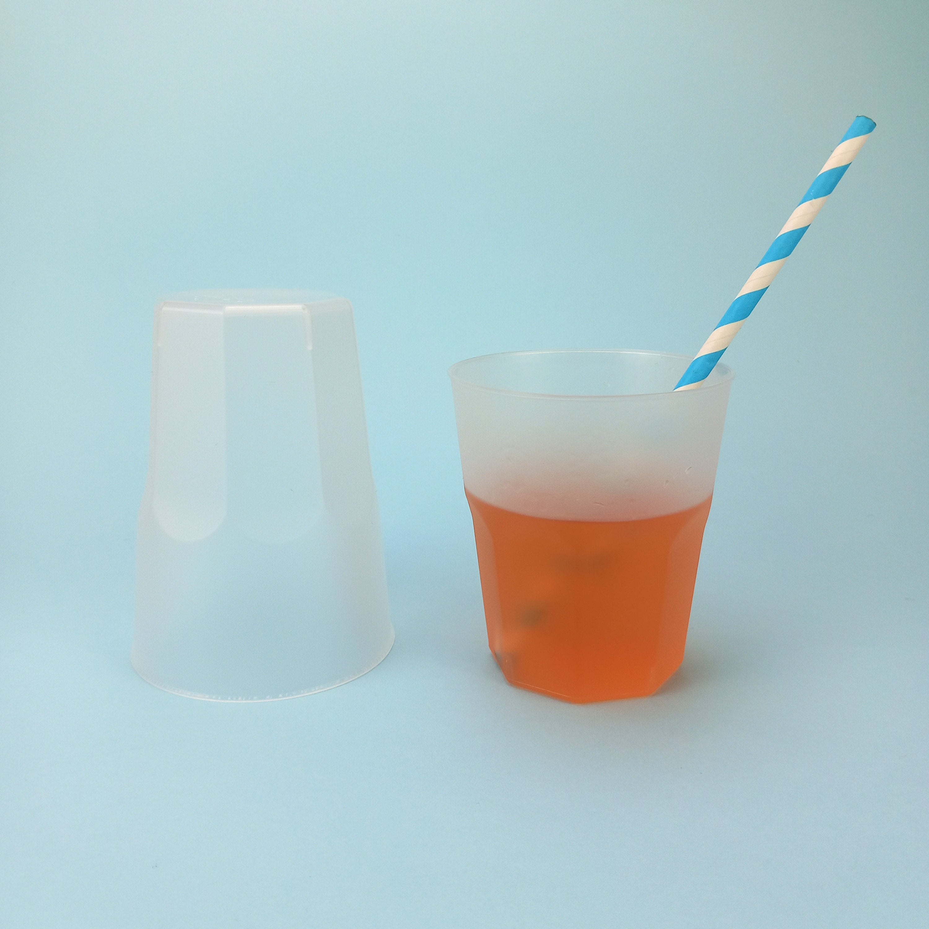 Bicchiere di plastica, opaco, monouso , uno capovolto ed uno pieno di te con cannuccia a righe bianco e azzurre 