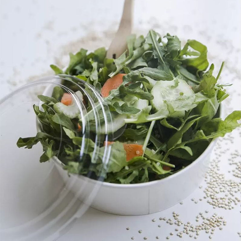 Ciotola di carta, bianca, con coperchio di plastica, su tavolino, piena di insalata 