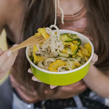 Ragazza che mangia cibo etnico da una ciotola di carta da asporto color verde