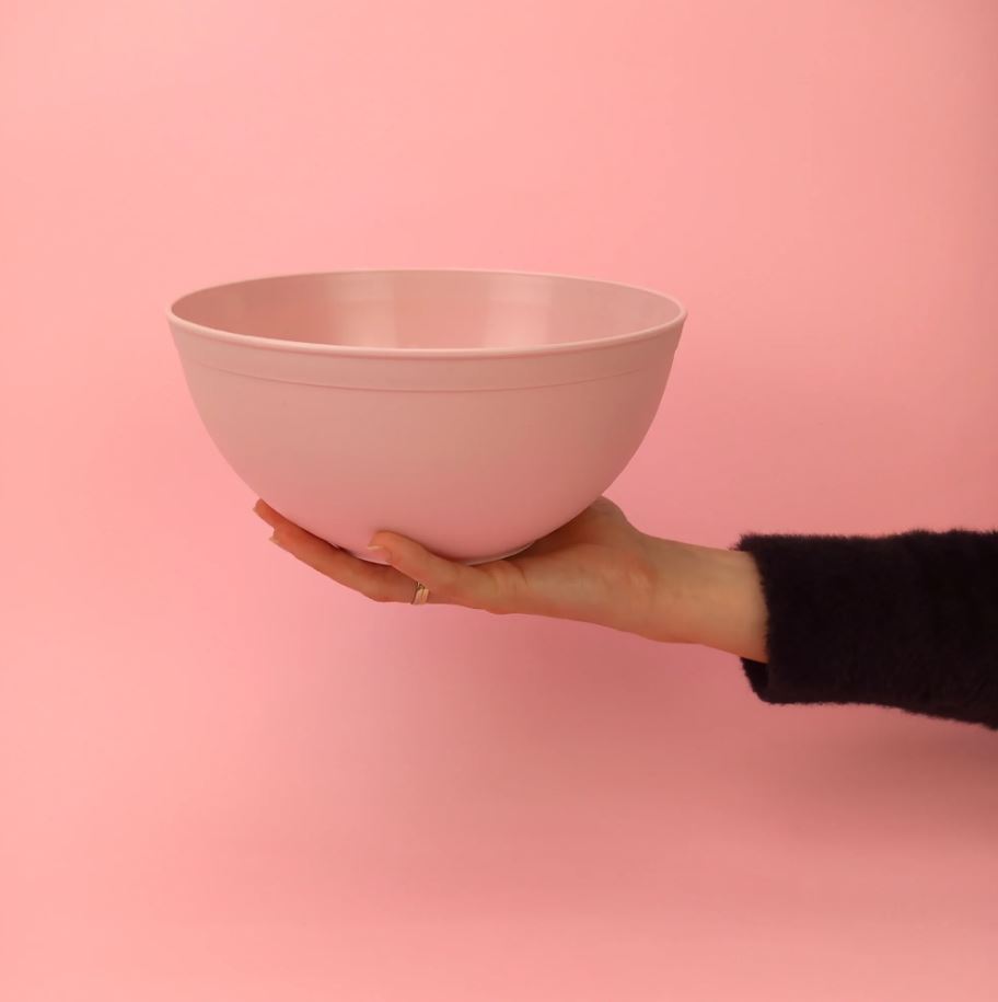 Ciotola rosa su sfondo rosa retta da una mano