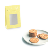 Confezione di carta gialla con finestra vicino a piatto con dei biscotti 
