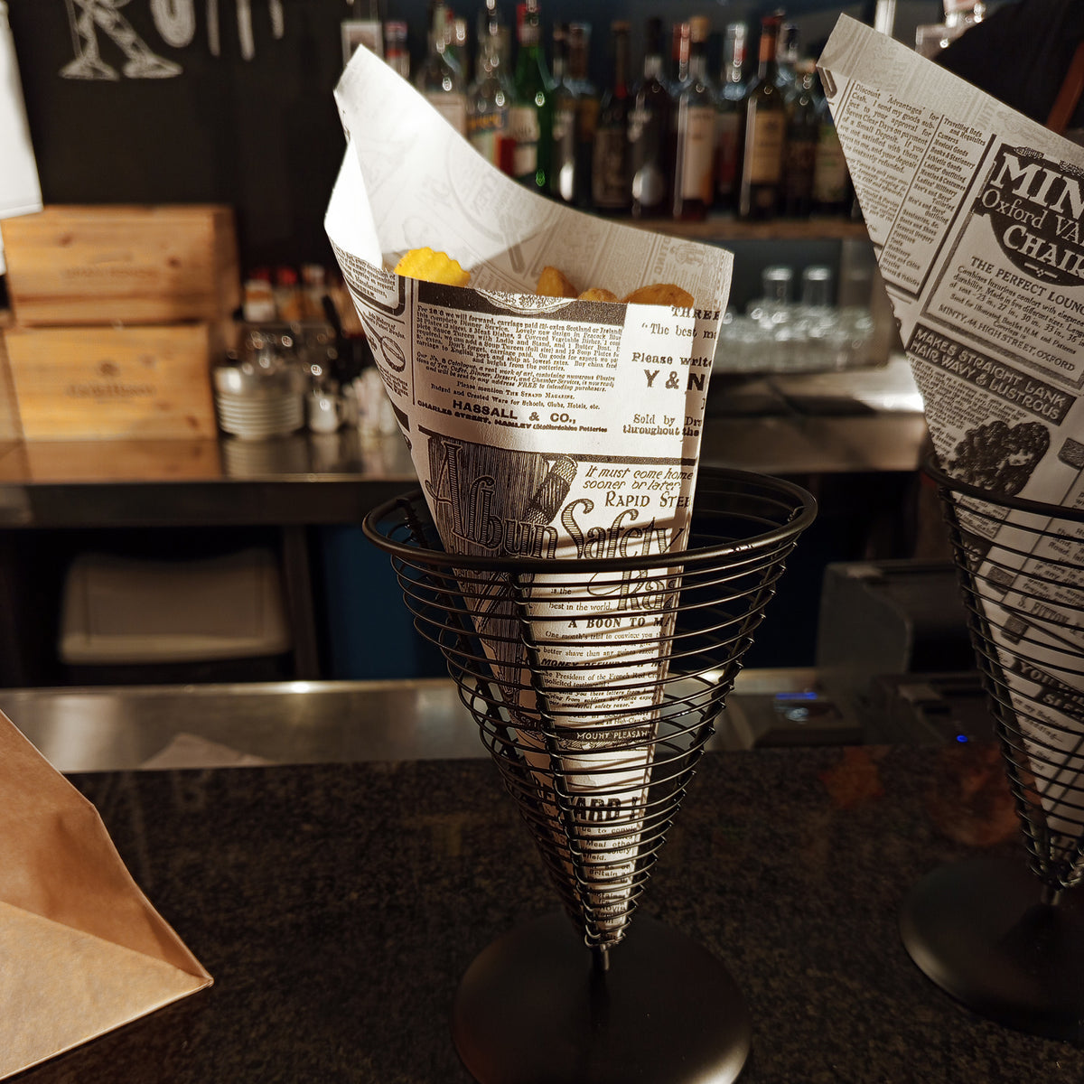 Cono per fritti su bancone di un bar con carta antigrasso a stampa giornale, ripieno di patatine