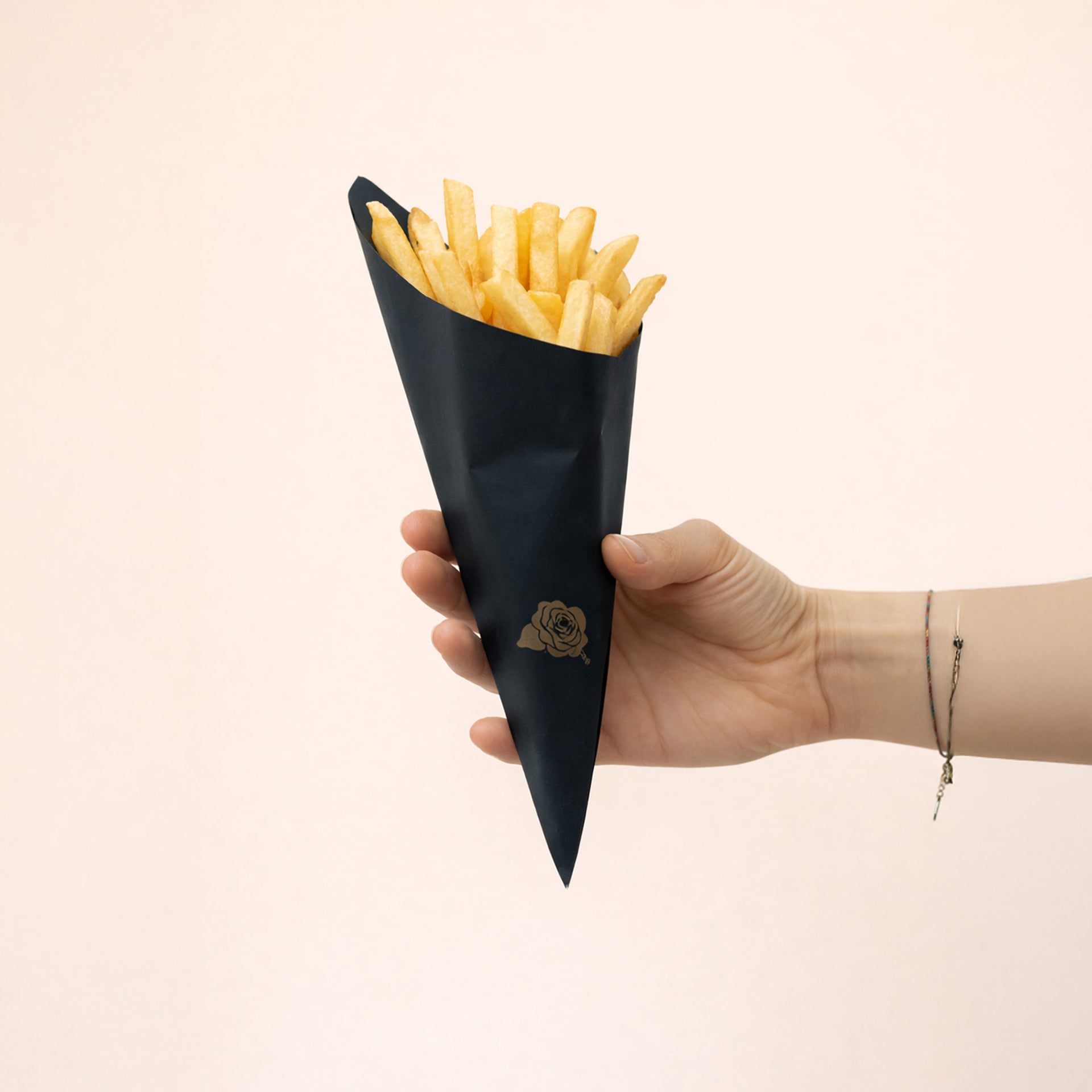 Mano che regge un cono in carta nera pieno di patatine fritte 