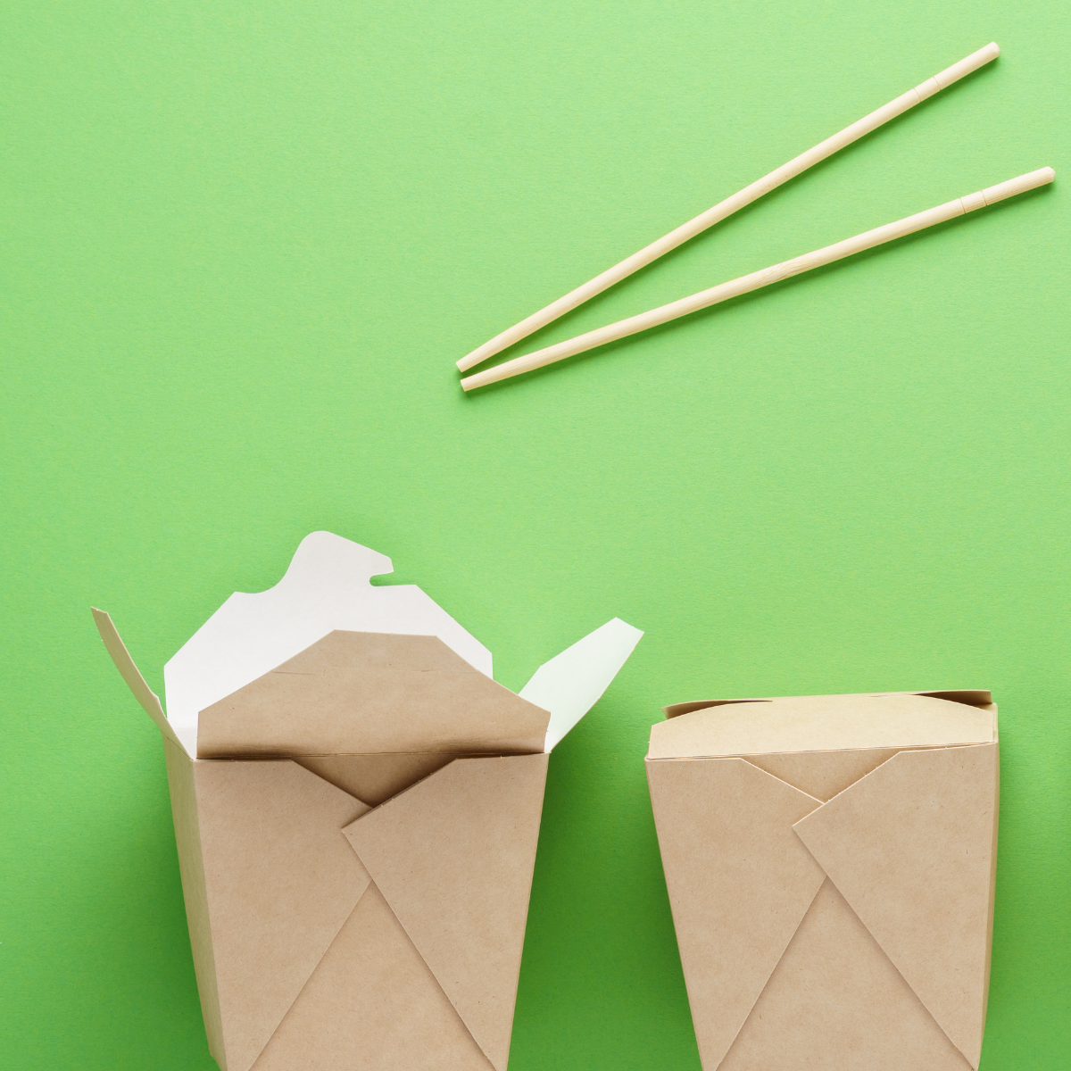 Contenitori per alimenti, da asporto cartoncino kraft avana. Uno aperto ed uno chiuso, su sfondo verde. Due bacchette posizionate sopra
