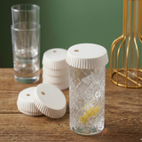 Bicchiere di gin tonic con coperchio di carta con foro e altri coperchi appoggiati vicino 