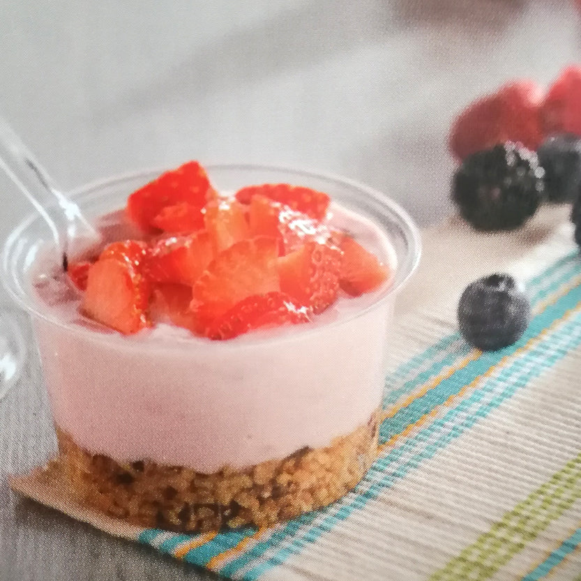 Coppetta in plastica trasparente, su tavolino, con muesli, yogurt e fragole