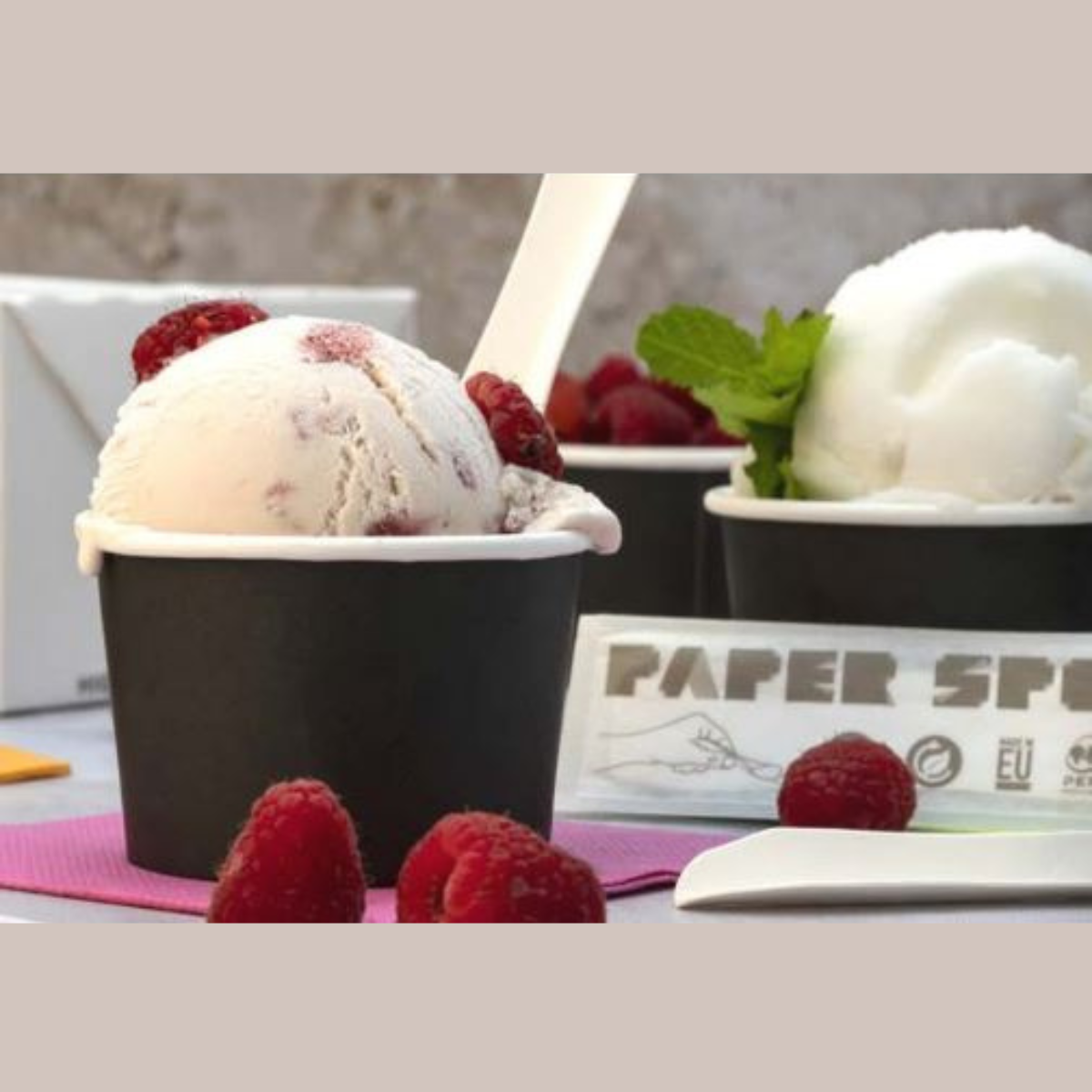 Coppetta gelato nera piena di gelato su un tavolo con altre coppette e dei lamponi