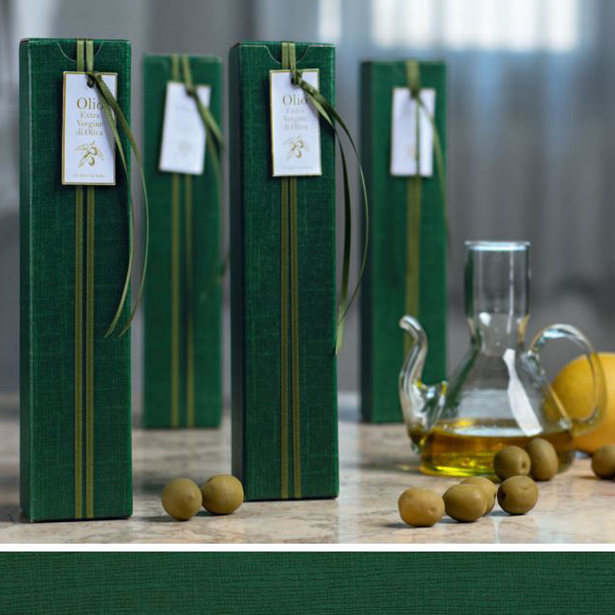 Scatole verdi per bottiglie di olio su tavolo vicino ad olive verdi e ad una ampolla con dell'olio