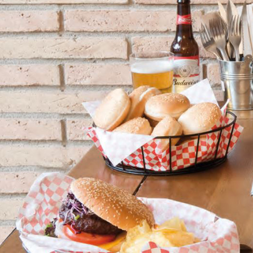 Tavolo di un bar con cestelli con carta alimentare a quadretti bianchi e rossi con panini ed una birra vicino 