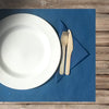 Apparecchiatura con tovaglietta blu e piatto bianco con posate di legno