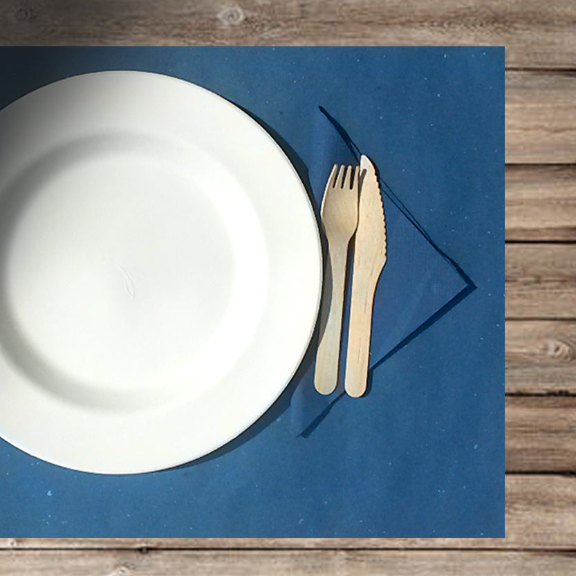 Apparecchiatura con tovaglietta blu e piatto bianco con posate di legno