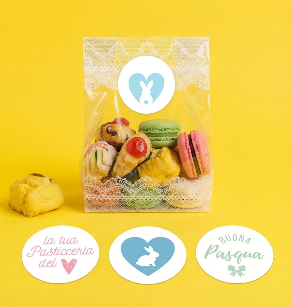 Sacchetto trasparente pieno di dolci chiuso con une etichetta pasquale tonda e tre etichette tonde pasquali appoggiate di fronte il sacchetto stesso