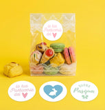 Sacchetto trasparente pieno di dolci chiuso con une etichetta pasquale tonda e tre etichette tonde pasquali appoggiate di fronte il sacchetto stesso