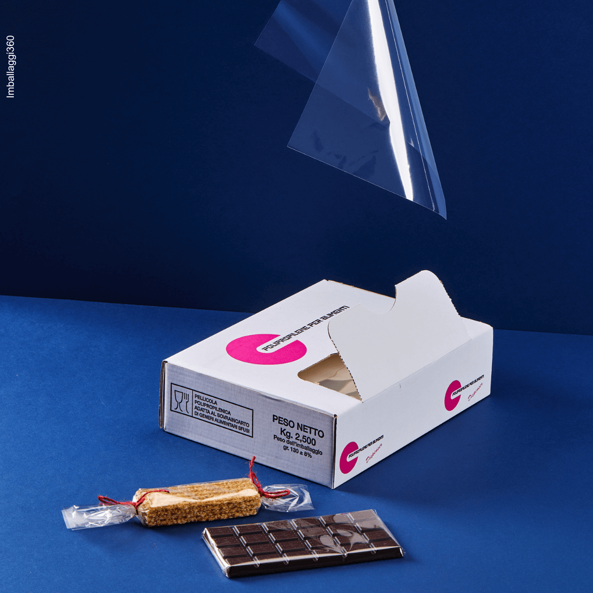 Foglio trasparente per alimenti che cade su tavolette di cioccolato avvolte dal foglio e sulla confezione stessa. Sfondo blu