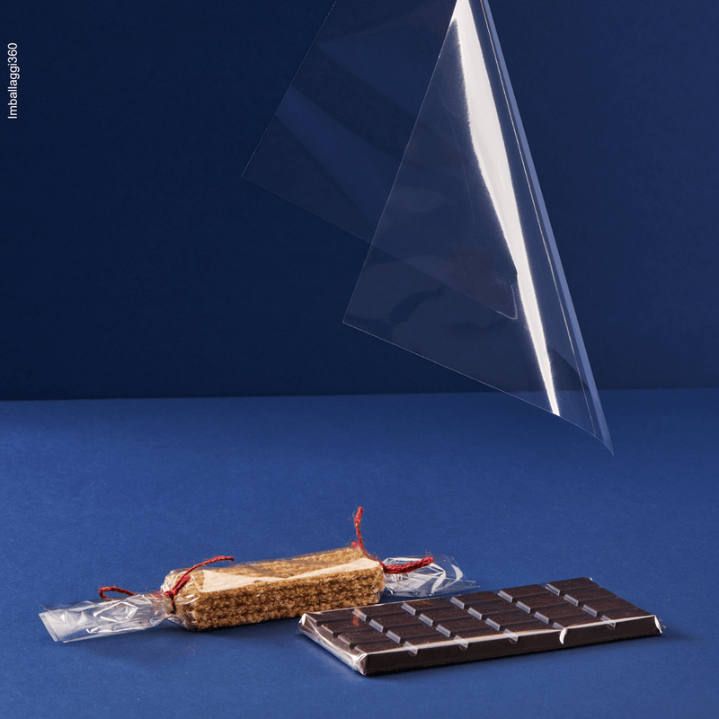 Foglio trasparente per alimenti che cade su tavolette di cioccolato avvolte dal foglio. Sfondo blu