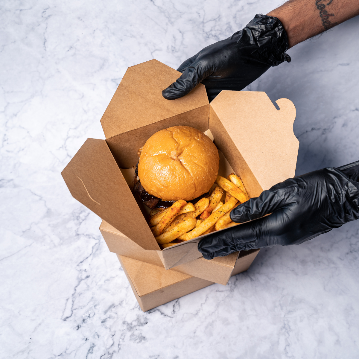 Mani, con guanti neri che aprono box di avana con dentro un panino e delle patatine