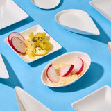 Piattino monoporzione in pola di cellulosa, varie misure. ripieno di finger food, accanto a piattini vuoti su sfondo azzurro