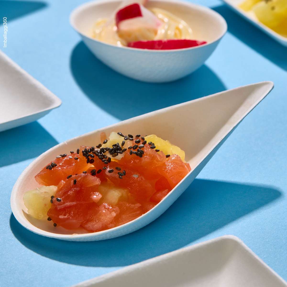 Piattino monoporzione in pola di cellulosa, varie misure. ripieno di finger food, accanto a piattini vuoti su sfondo azzurro. Dettaglio
