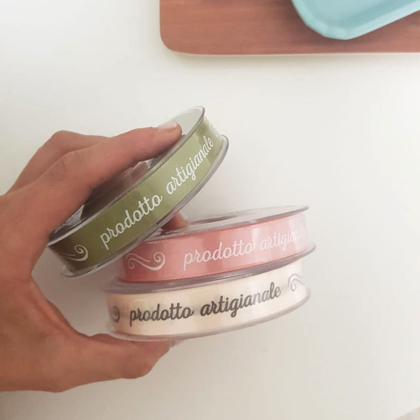 Nastri con scritta prodotto artigianale, di tre colori diversi, retti da una mano 