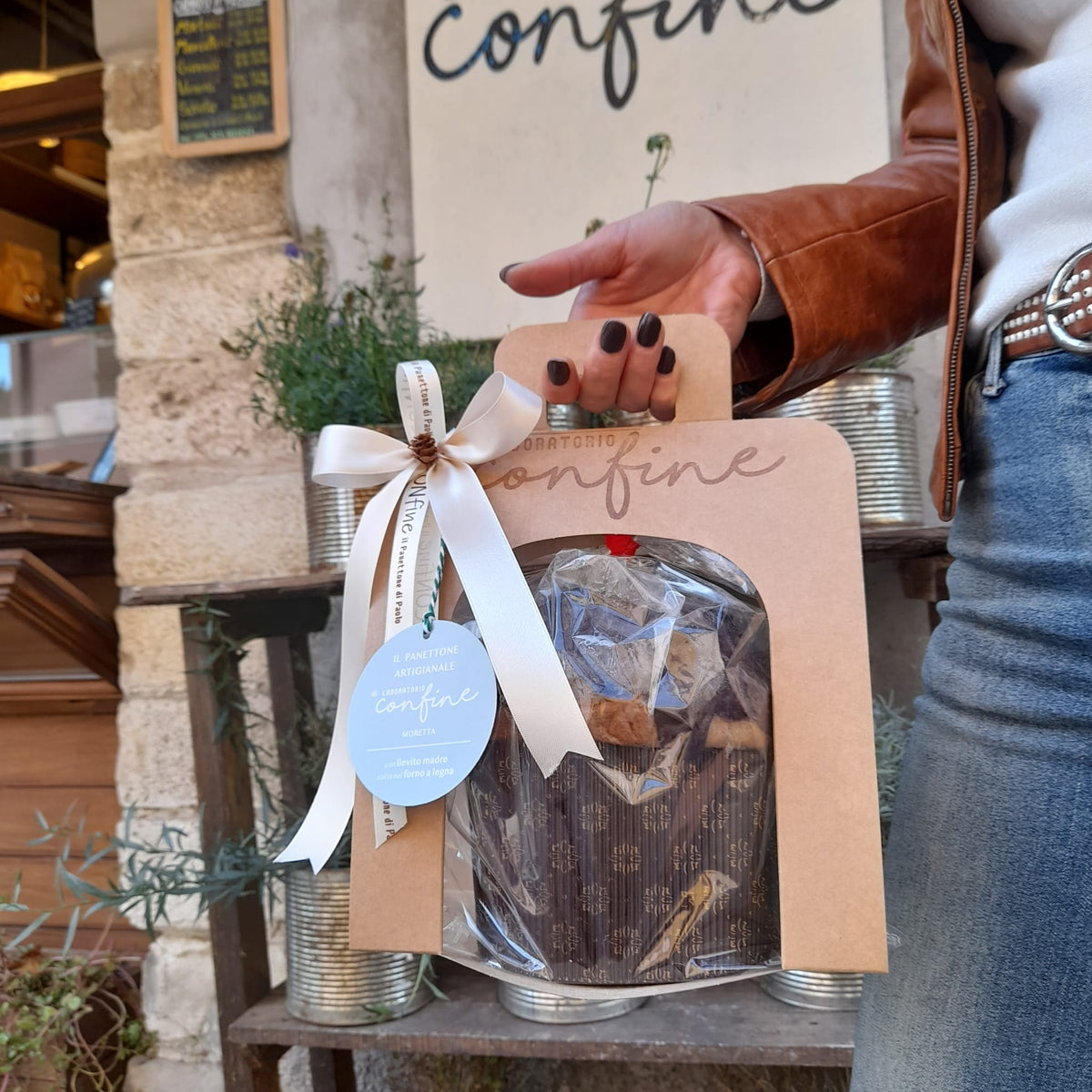 Mano che regge, all'uscita di un negozio, un panettone nella sua confezione porta panettone con finestra 