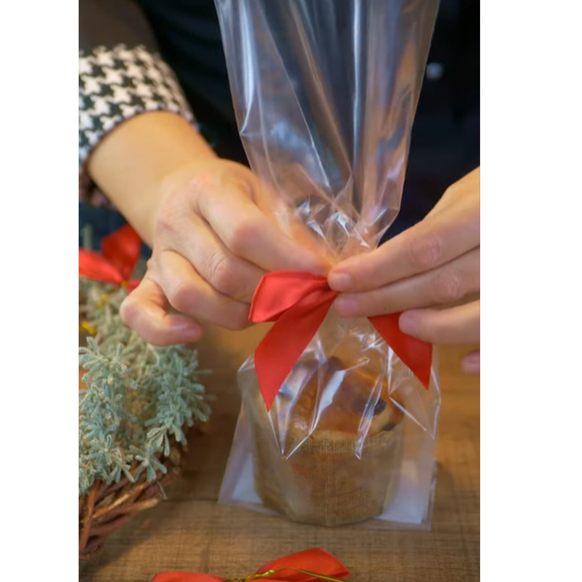 Mani che infiocchettano un sacchetto di plastica trasparente con dentro mini panettone 