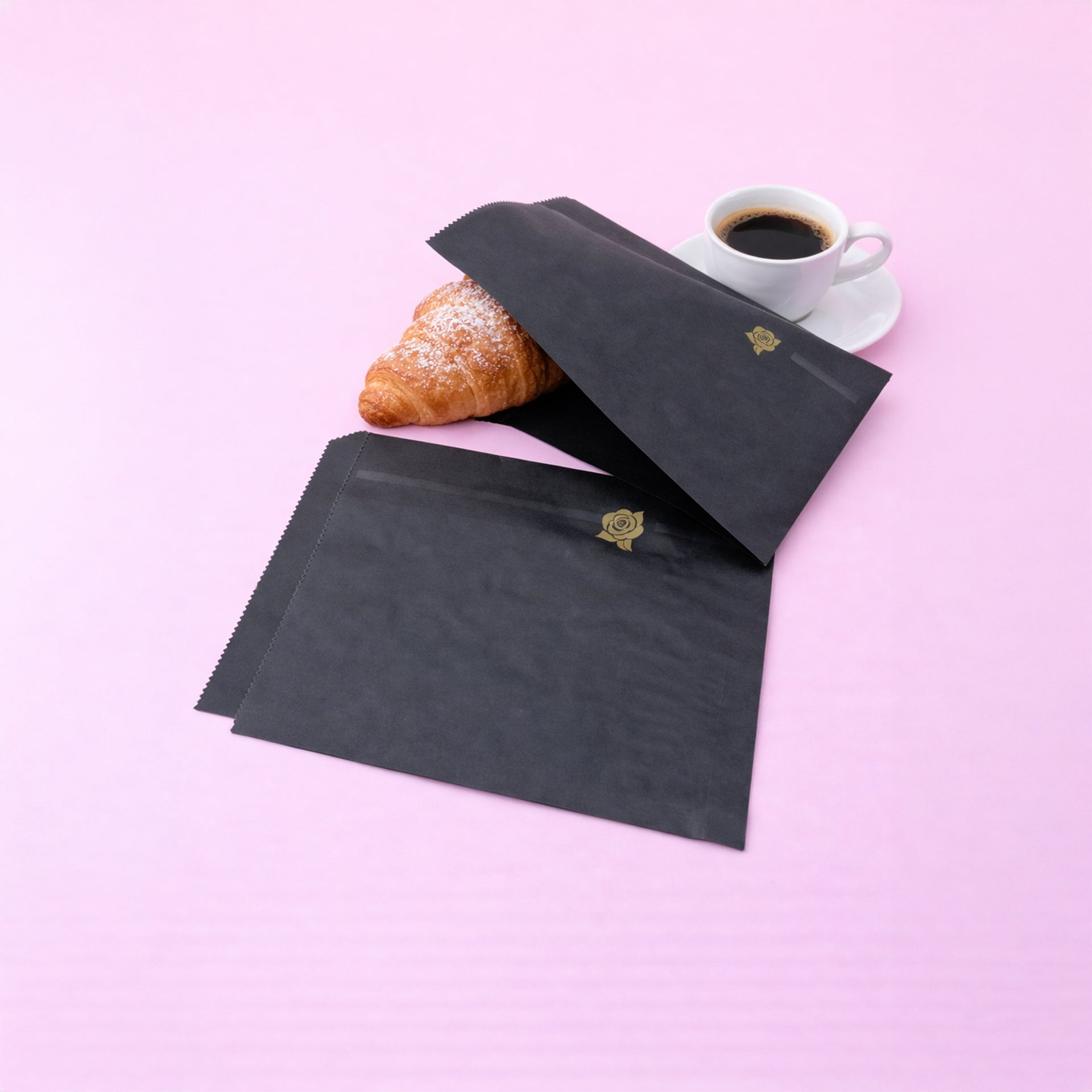Sacchetti, due, di carta neri, uno vuoto ed uno con un cornetto, vicino ad una tazza di caffe