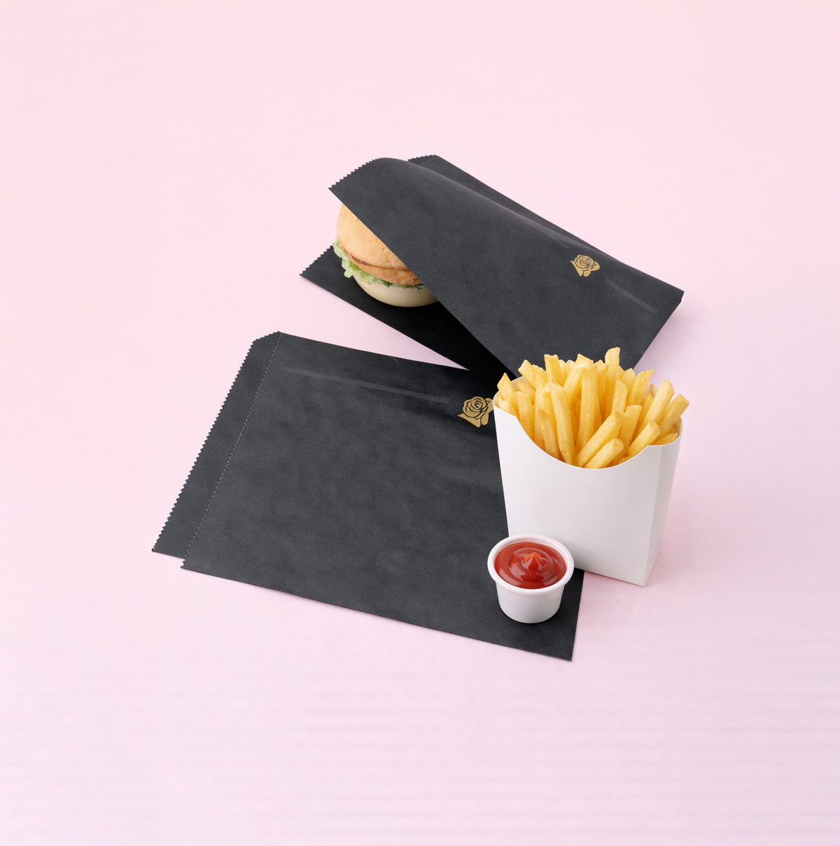 Sacchetti, due, di carta neri, uno vuoto ed uno con un hamburger, vicino a patatine fritte e bicchierino di salsa ketchup  