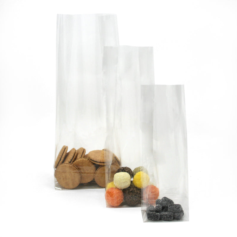 Sacchetti di plastica trasparenti a fondo quadro, tre misure diverse, pieni di biscotti, caramelle e liquerizia 