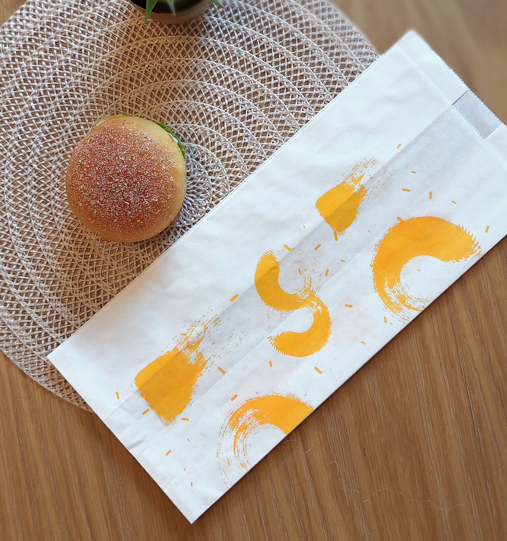 Sacchetto bianco per il pane con macchie di colore giallo, su un tavolo sotto a un panino