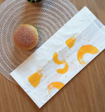 Sacchetto bianco per il pane con macchie di colore giallo, su un tavolo sotto a un panino