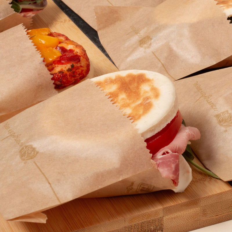 Sacchetti antigrasso color avana, su un tavolo, ripieni di panini