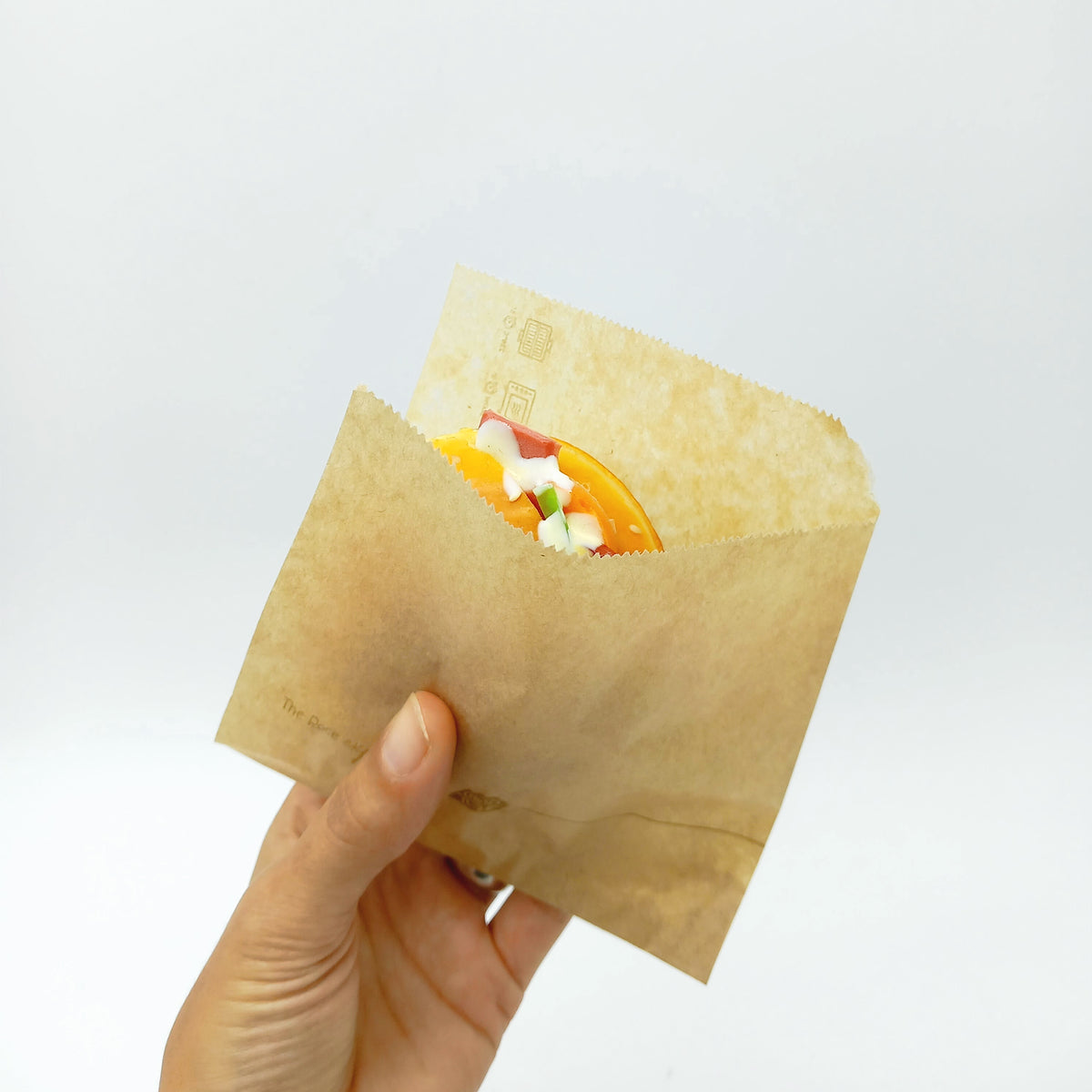 Sacchetto color avana, con dentro un panino, retto da una mano