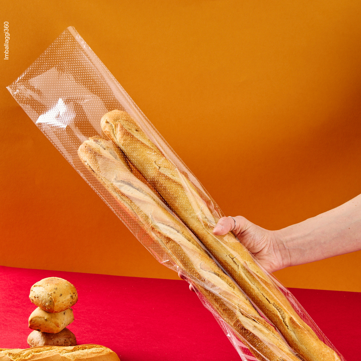 Sacchetto microforato , mostrato con del pane, dentro, retto da una mano. Sfondo rosso