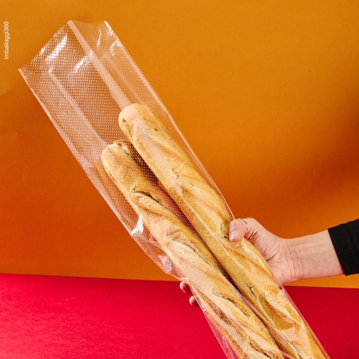 Sacchetto microforato , mostrato con del pane, dentro, retto da una mano. Sfondo rosso