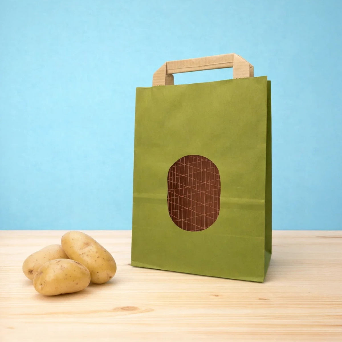 Sacchetto verde per patate con finestra con retina su tavolo di legno vicino a tre patate 