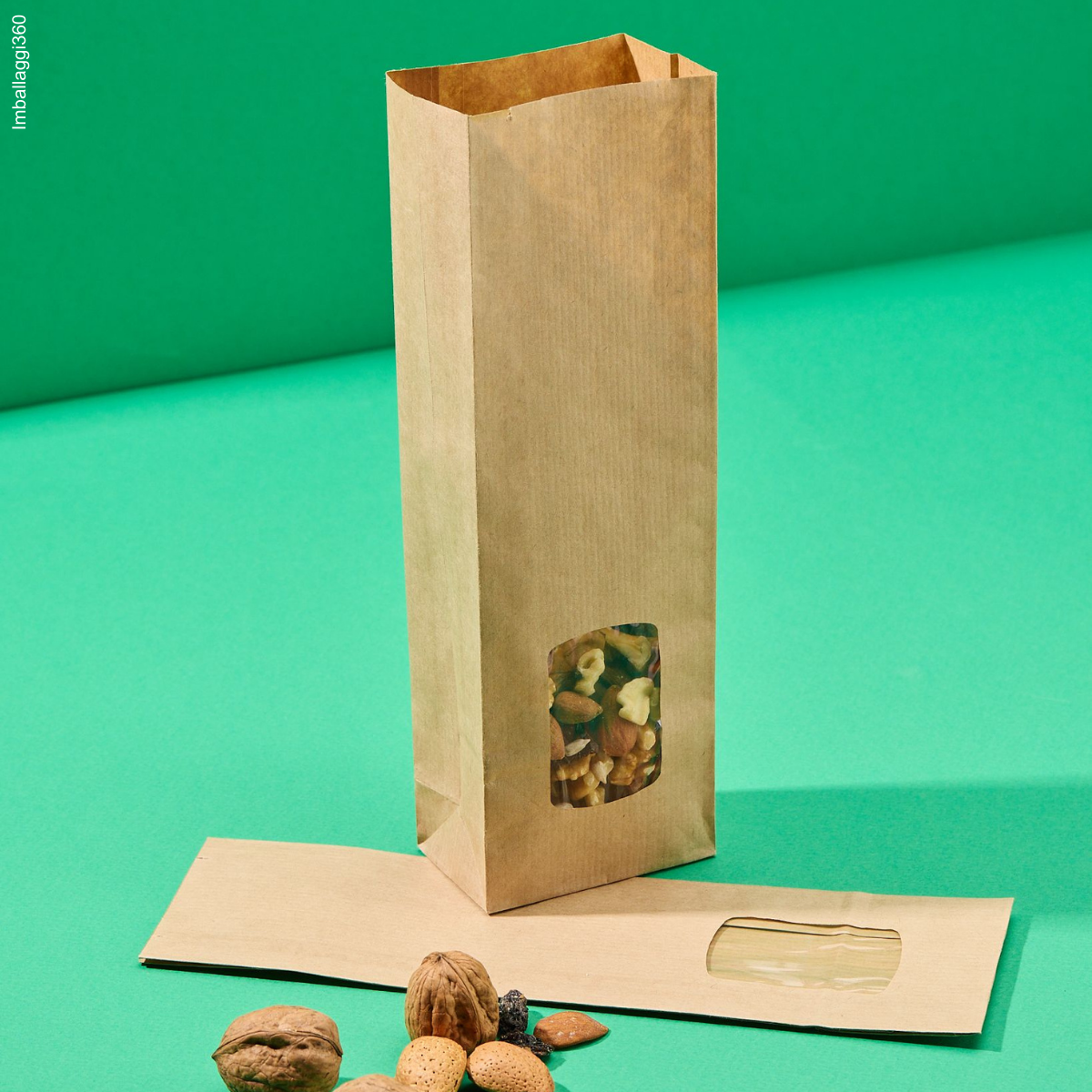 Sacchetti coloro avana con finestra, per biscotti, diverse dimensioni: uno pieno con frutta secca ed uno vuoto, chiuso steso. Sfondo verde