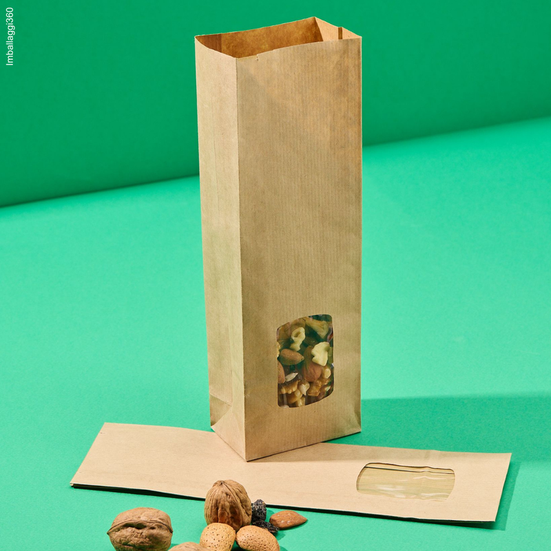 Sacchetti coloro avana con finestra, per biscotti, diverse dimensioni: uno pieno con frutta secca ed uno vuoto, chiuso steso. Sfondo verde