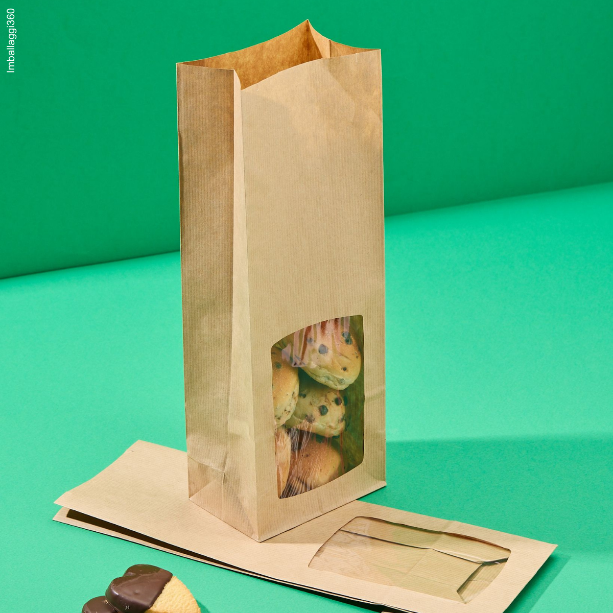 Sacchetti coloro avana con finestra, per biscotti, : uno pieno con biscotti, uno vuoto e chiuso steso. Sfondo verde