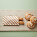 Vista dall'alto di tagliere con sopra tre pagnotte e una busta a righe di carta con dentro due filoni di pane 