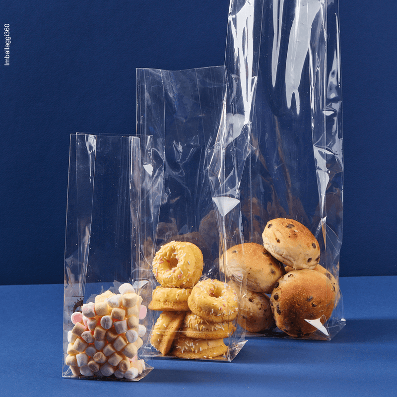 Sacchetto a fondo quadro, trasparente, ripieno di caramelle e dolci varie misure. Sfondo blu 