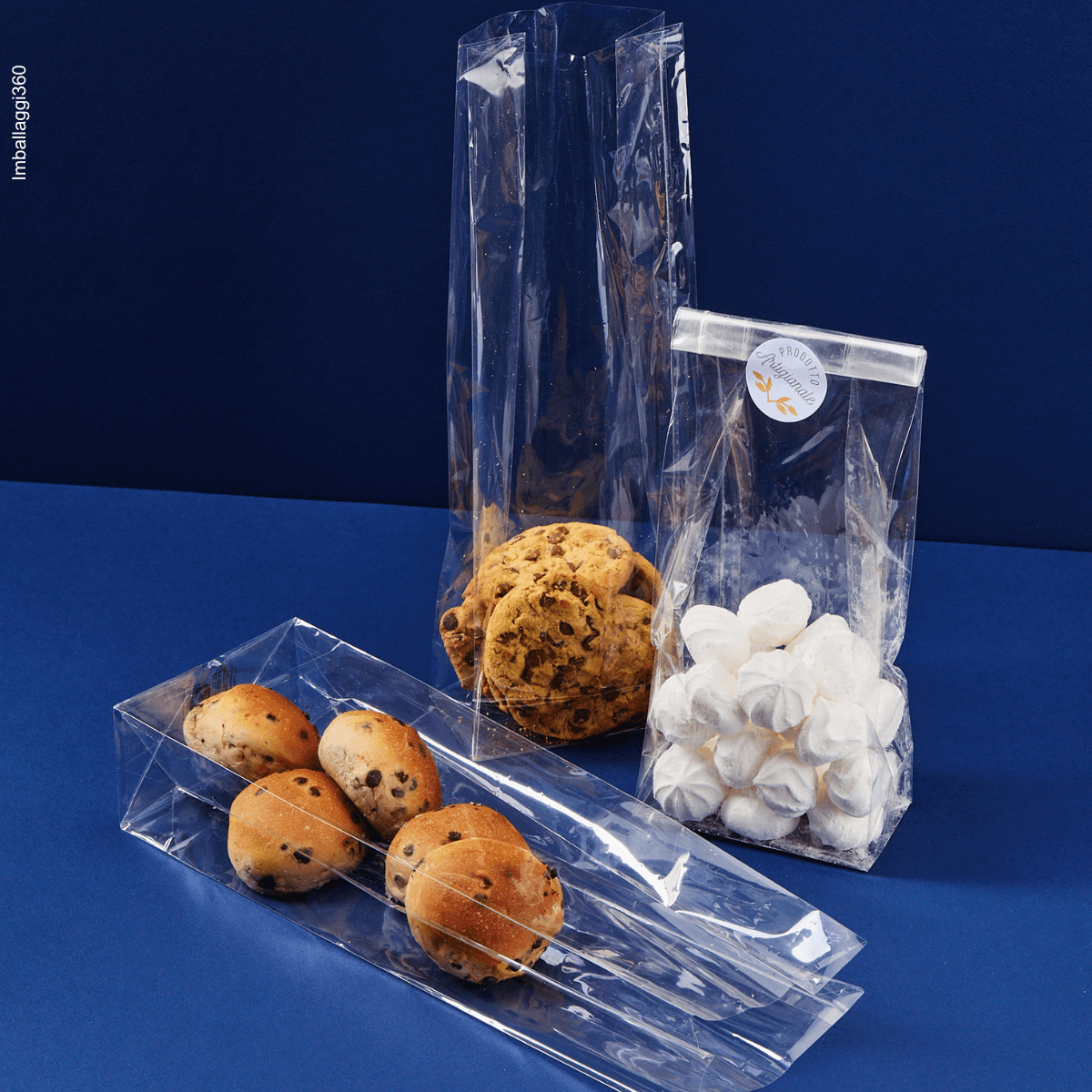 Sacchetto trasparente, fondo quadro, ripieno di dolci, diverse misure, uno steso, uno chiuso con etichetta prodotto artigianale. Sfondo blu