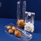Sacchetto trasparente, fondo quadro, ripieno di dolci, diverse misure, uno steso, uno chiuso con etichetta prodotto artigianale. Sfondo blu