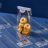 Sacchetto a fondo quadro, trasparente, ripieno di dolci, chiuso con etichetta, su sacchetti chiusi e stesi. Sfondo blu 