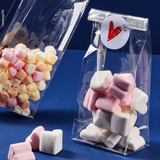 Sacchetto trasparente, fondo quadro, ripieno di dolci, dettaglio di uno aperto e centralità di uno chiuso con etichetta cuore . Sfondo blu