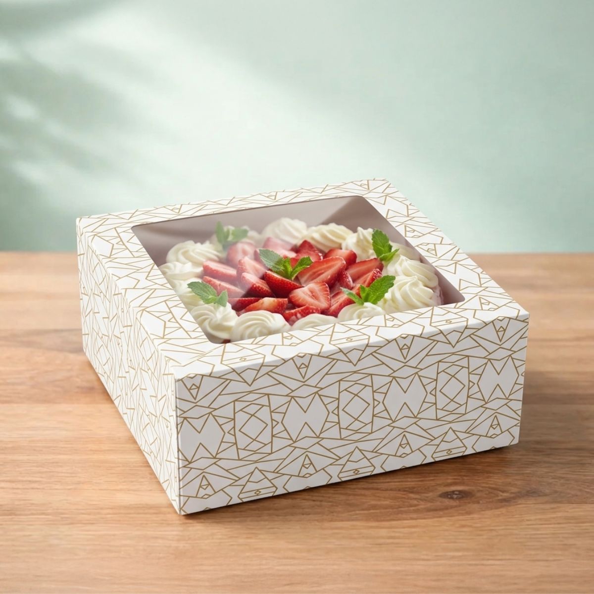 Scatola porta torte bianca con grafiche geometriche dorate, con finestra, su un tavolo di legno, con dentro una torta panna e fragole 