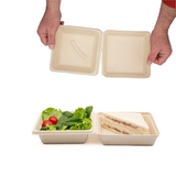 Scatola da asporto mostrata aperta da due mani e piena con insalata e panino 