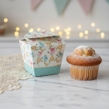 Scatola floreale per muffin con vicino un muffin, su un tavolo 