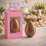 Scatola porta uova di cioccolato fucsia con finestra con un uovo di cioccolato dentro ed uno fuori, su un tavolo con tanti elementi pasquali e primaverile 